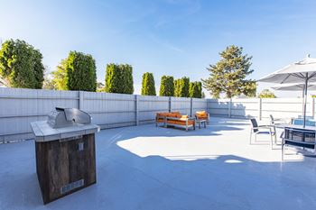 the terrace has a grill and seating area with tables and chairs at The Lakes Apartments, Washington, 98837